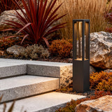 LED bollard garden light with vertical light strips, positioned beside colorful plants for stylish outdoor lighting